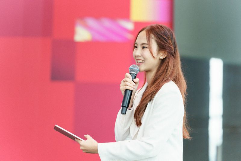 คุณเขมรินทร์ วีระเผ่า พิธีกรของงาน ถือไมโครโฟนและยิ้มขณะเปิดงาน