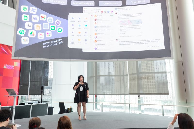 คุณเจียหลิงบรรยายบนเวที จอด้านบนแสดงสไลด์ All the apps you need in one Lark