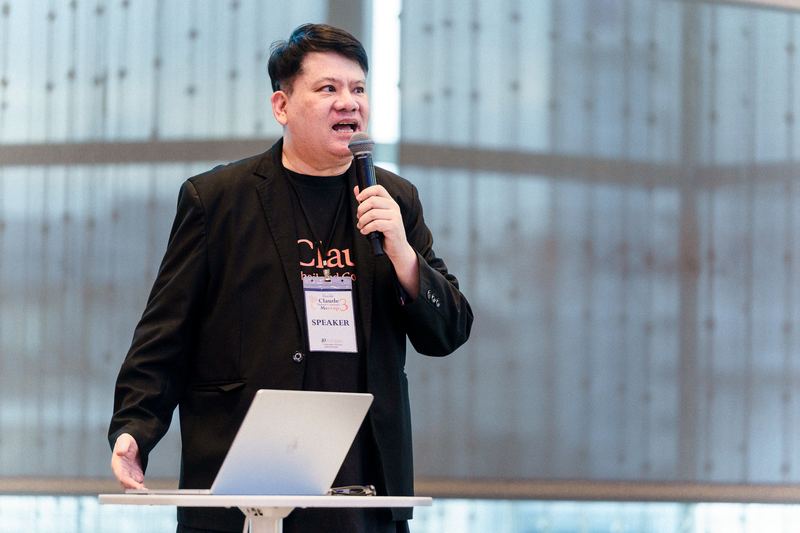 คุณปรเมศวร์ มินศิริ ถือไมโครโฟนบรรยายหลังโพเดียมที่วางโน้ตบุ๊ก